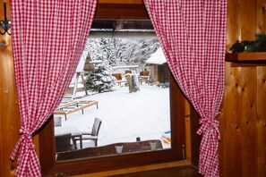A window view of a snowy outdoor area with a wooden cabin, a bench, and a tree. - Alpine Lodge Goska Ravan Rooms (Radovljica)