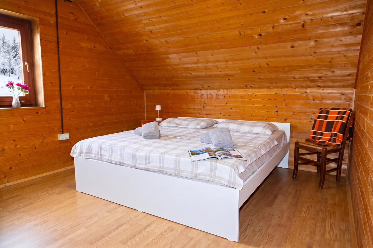 A wooden cabin bedroom with a bed, a window, a chair, and a lamp.