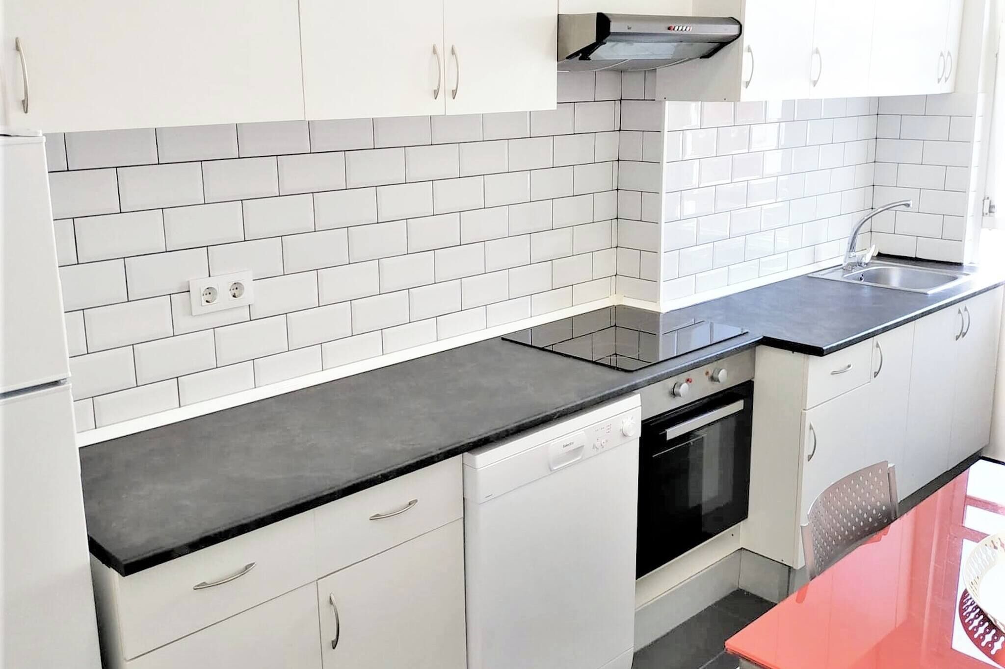 A kitchen with white cabinets, a black countertop, a built-in oven, and a stainless steel sink.