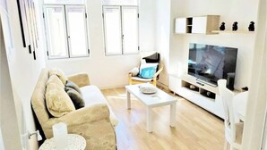Uma sala de estar com sofá, mesa de centro, televisão e uma poltrona.