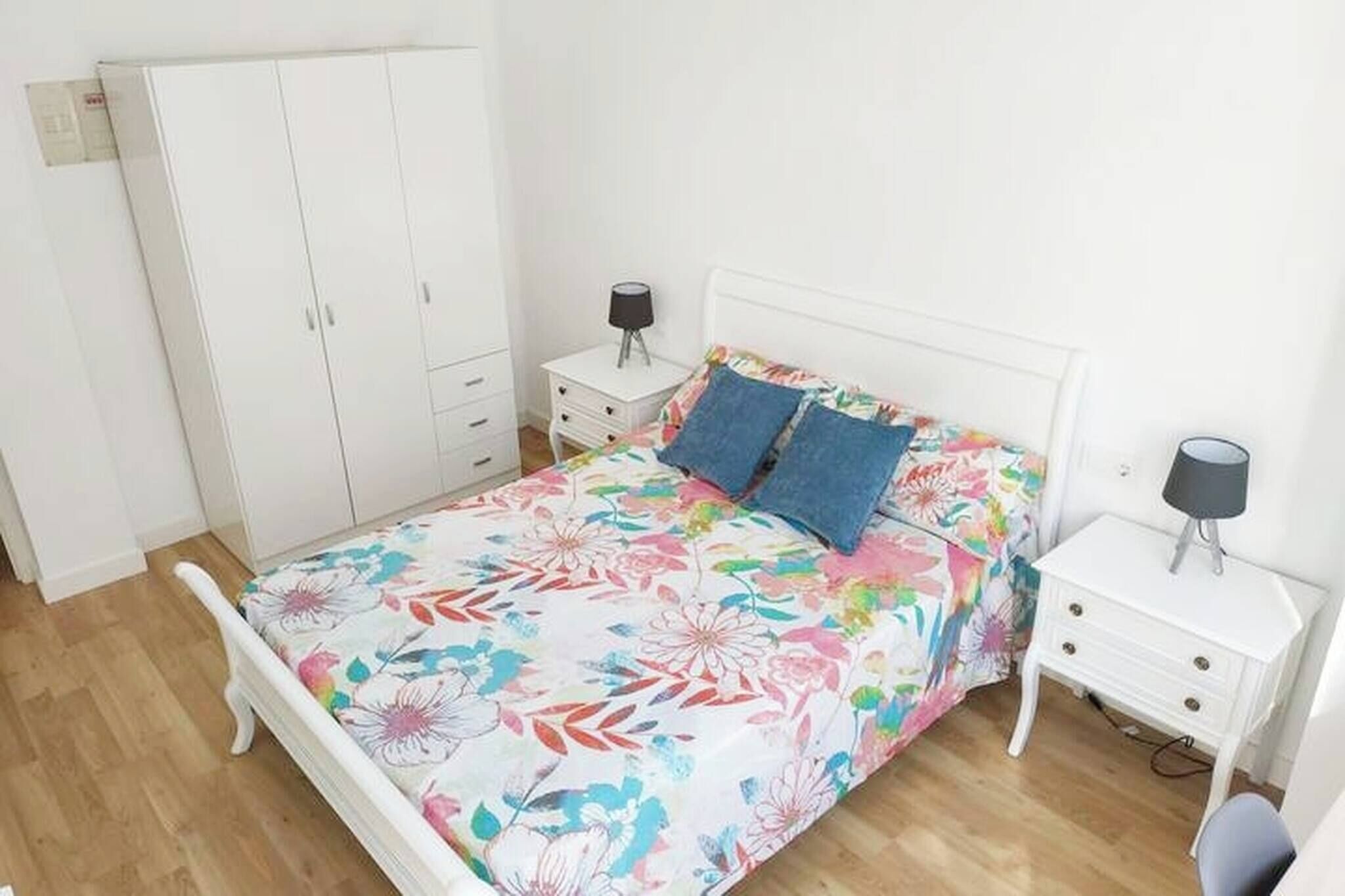 Un dormitorio con una cama, dos mesitas de noche, un armario y una mesilla.