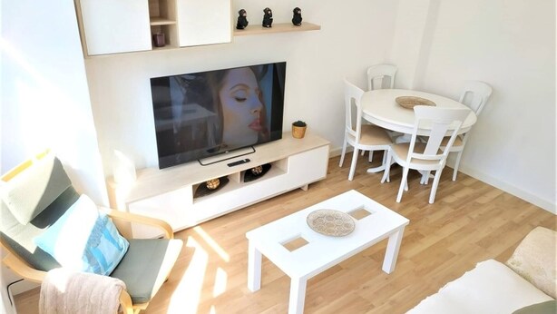 Uma sala de estar moderna com televisão de tela plana, uma mesa de jantar com cadeiras, um sofá e uma mesa de centro.