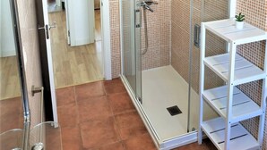 Um banheiro com box de vidro, pia branca com uma planta e parede revestida em azulejos.
