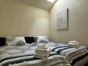 Ein Hotelzimmer mit zwei Betten, jedes mit einem gemusterten Bettbezug und Kissen, sowie einem an der Wand befestigten Schild mit Text.