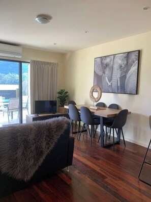 Una sala de estar moderna con un televisor de pantalla plana, una mesa de comedor con sillas, un cuadro abstracto grande y un otoman tapizado en piel.