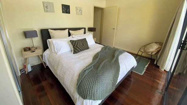 A bedroom with a bed, bedside tables, a chair, and a door. - Halls Gap Escape Townhouse 4 (Halls Gap)