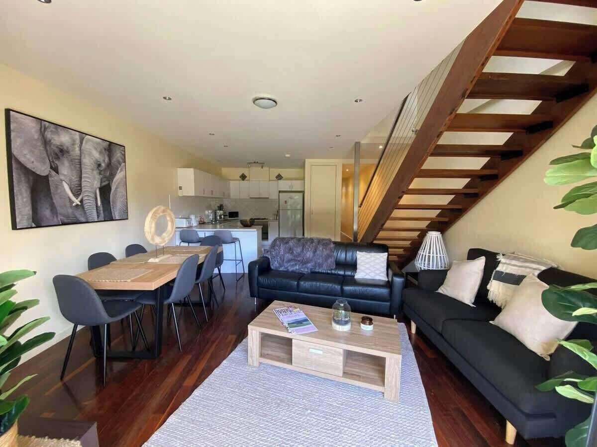 Ein modernes Wohnzimmer mit Essbereich, einer schwarzen Ledersofa, einem Holztisch und einer Treppe.
