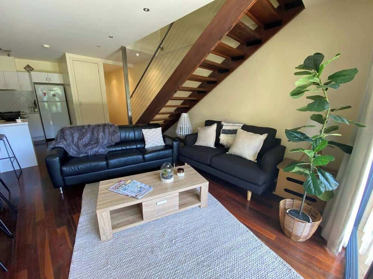 A modern living room with a sofa set, a coffee table, and a staircase.