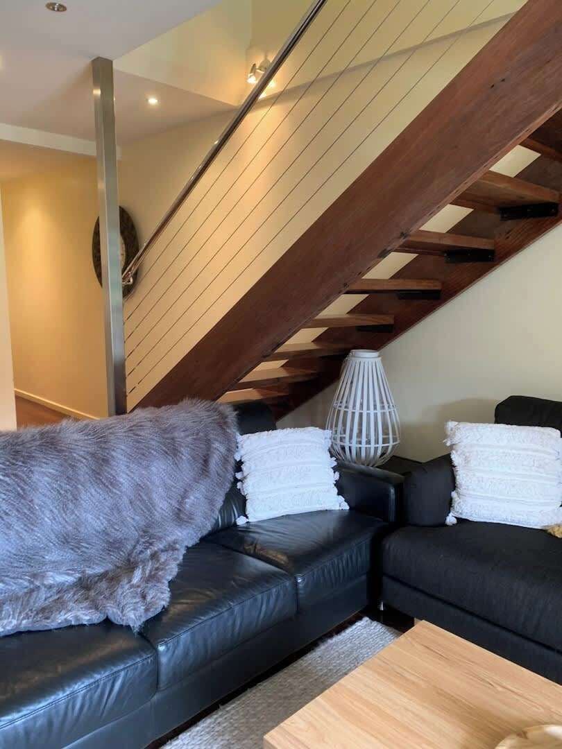Ein modernes Wohnzimmer mit einem schwarzen Ledersofa, einem Holzbalken an der Decke und einer weißen Stehlampe.
