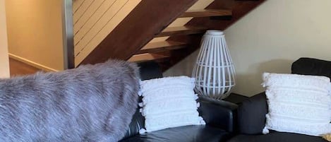 Ein modernes Wohnzimmer mit einem schwarzen Ledersofa, einem Holzbalken an der Decke und einer weißen Stehlampe.
