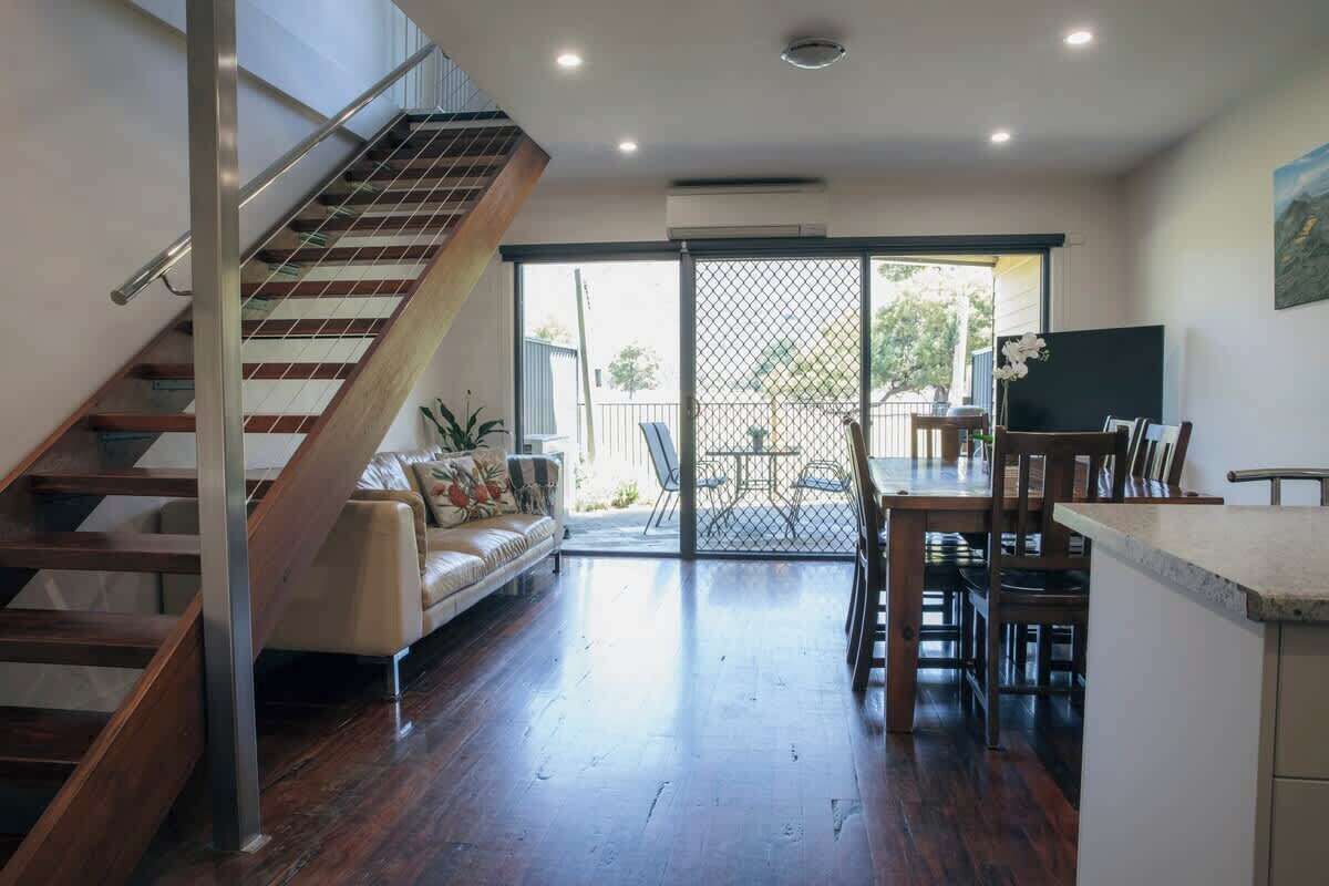 A modern interior with a staircase, a sofa, a dining area, and a view through a sliding door.