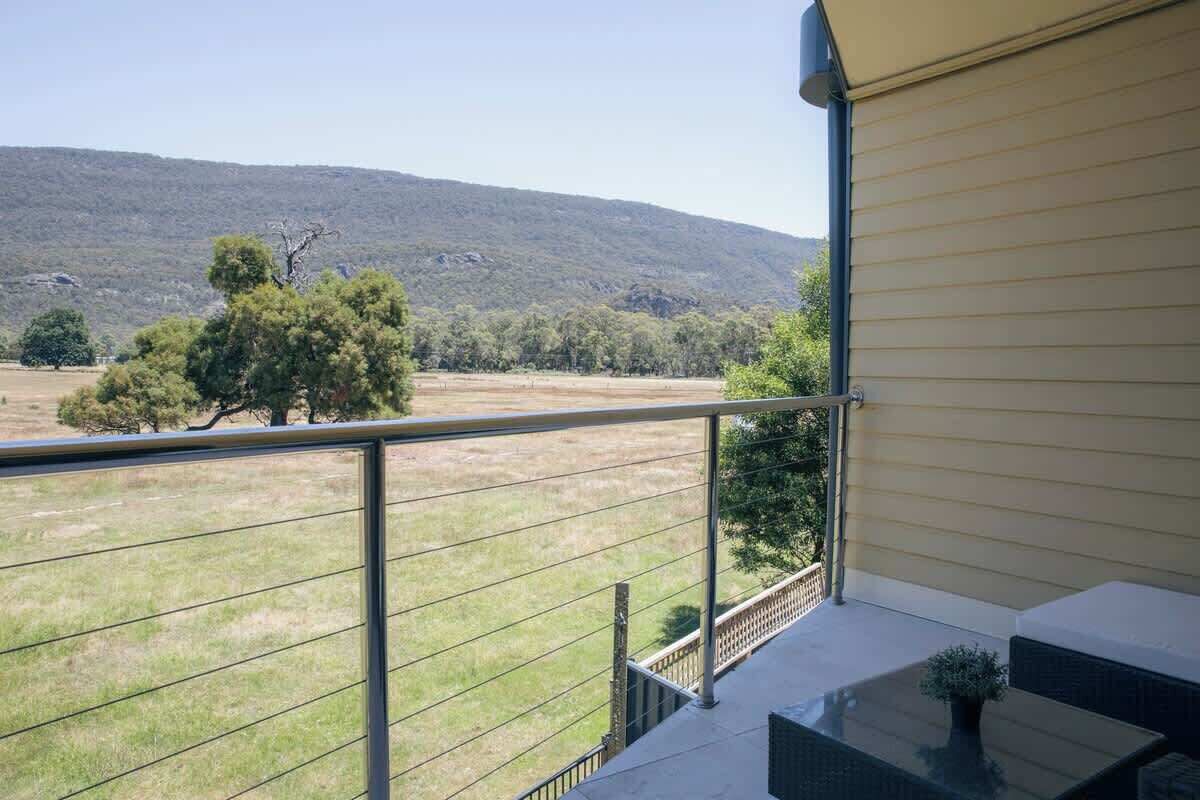 A balcony with a metal railing overlooking a grassy field and trees, with a building in the background.