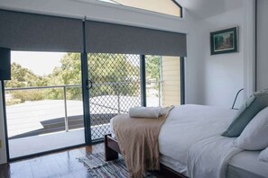 Un dormitorio con un amplio ventanal corredizo que da a un balcón, una cama con ropa de cama blanca y un cuadro en la pared.
