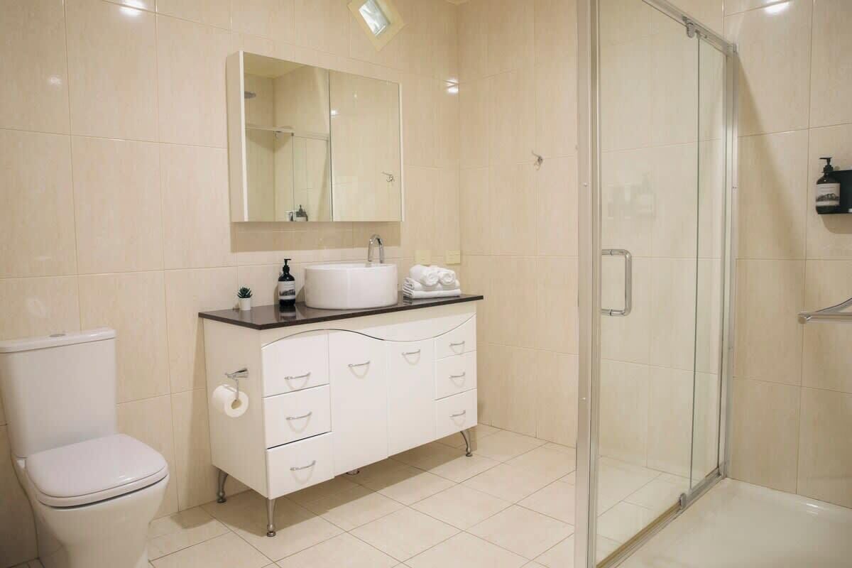 Ein Badezimmer mit Toilette, Waschbecken, Spiegel, Dusche und einem Schrank.