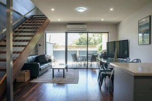 A modern living space with a staircase, a sofa, a coffee table, a dining area, and a TV. - Kodama Halls Gap Townhouse (5) (Halls Gap)