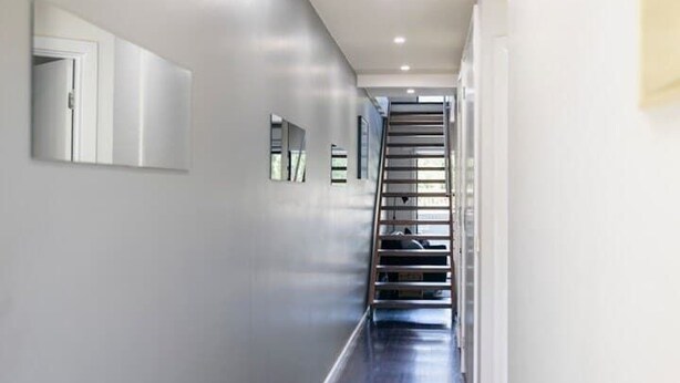Ein Flur mit einer Treppe, die zu einer anderen Etage führt, einer Tür links und einer Wandleuchte.