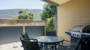 Eine Terrassengruppe im Freien mit rundem Tisch und Stühlen, einem Grill und Blick auf Hügel.