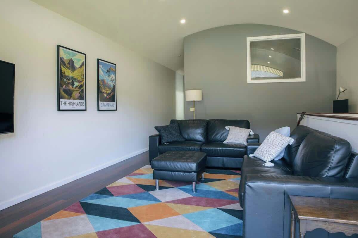 Ein Wohnzimmer mit einer schwarzen Ledersofa, einem farbenfrohen geometrischen Teppich und zwei gerahmten Bildern an der Wand.