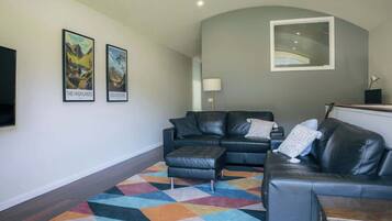 Ein Wohnzimmer mit einer schwarzen Ledersofa, einem farbenfrohen geometrischen Teppich und zwei gerahmten Bildern an der Wand.