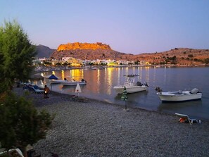 A coastal scene with boats docked at a marina, a hill with a fort-like structure, and buildings along the shore. - The Village Retreat
Live like a local! (Malonas)