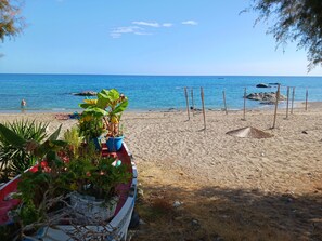 A beach with a row of potted plants, a red and white boat, and a clear blue sky. - The Village Retreat
Live like a local! (Malonas)