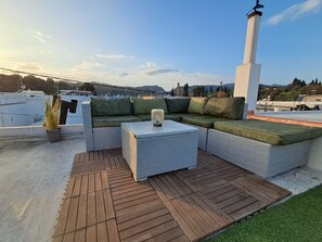 A rooftop terrace with a sectional sofa, a small table, and a potted plant. - The Village Retreat
Live like a local! (Malonas)