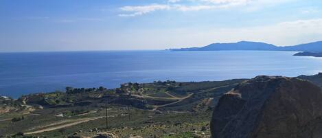 A coastal landscape with a clear view of the sea, rocky terrain, and distant hills.