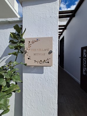 A sign on a white wall indicating 'The Village Retreat' with a decorative floral design. - The Village Retreat
Live like a local! (Malonas)