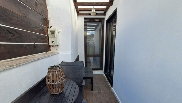 A narrow outdoor patio with a wooden table and a bench, a wicker basket, and a wall-mounted light fixture. - The Village Retreat
Live like a local! (Malonas)