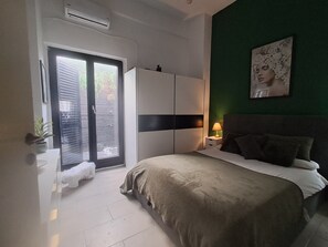 A bedroom with a bed, a wardrobe, a nightstand with a lamp, a green wall, and a window with blinds. - The Village Retreat
Live like a local! (Malonas)