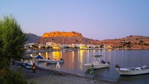 A coastal town with a fortified hill, boats docked along the shore, and a clear sky. - The Village Retreat
Live like a local! (Malonas)