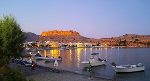 A coastal town with a fortified hill, boats docked along the shore, and a clear sky. - The Village Retreat
Live like a local! (Malonas)