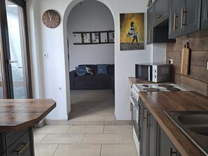 Una cucina con microonde, fornello e piano di lavoro in legno. Sul muro c'è una sveglia e un quadro sopra il fornello.