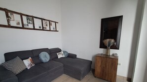 A living room with a grey sectional sofa, a wooden side table, a mirror, and a wall-mounted picture frame. - The Village Retreat
Live like a local! (Malonas)