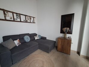 A living room with a grey sectional sofa, a wooden side table, a mirror, and a wall-mounted picture frame. - The Village Retreat
Live like a local! (Malonas)