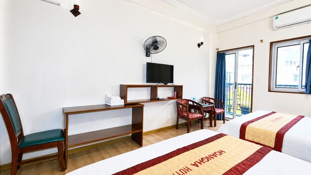 Una camera d'albergo con un letto, una scrivania, una sedia, una televisione e una finestra con tende.