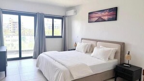 A bedroom with a large bed, a nightstand, a lamp, and a painting on the wall. - Bright two-bedroom apartment with a balcony (Dakar)