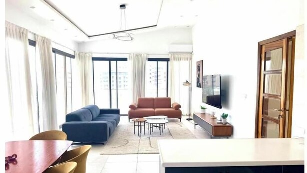 A modern living room with a sofa, a dining table with chairs, a TV, and a kitchen area with cabinets. - Bright two-bedroom apartment with a balcony (Dakar)