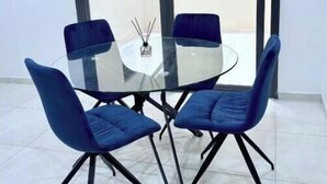 A modern dining area with a glass table and four blue chairs.