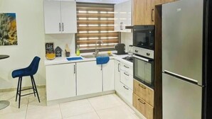 A modern kitchen with white cabinets, a wooden countertop, a stainless steel refrigerator, and a blue bar stool.