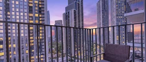 A balcony with a view of high-rise buildings, a chair, and a small plant.