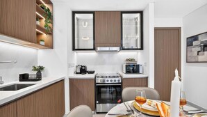 Una cocina compacta con electrodomésticos integrados, un comedor con una mesa lista para dos personas y un mueble con plantas decorativas.