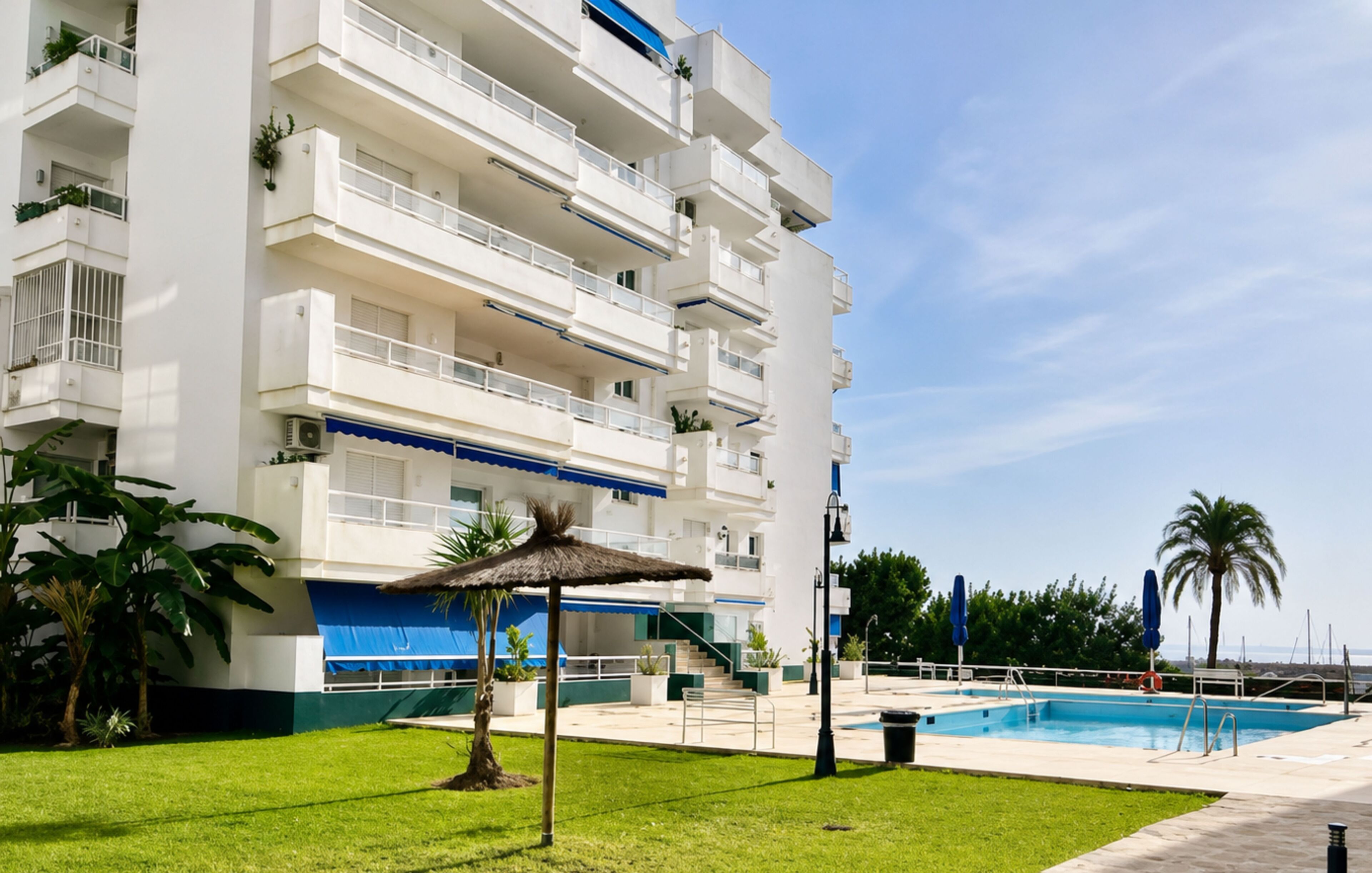 A multi-story hotel with a swimming pool, outdoor seating, and a clear sky.