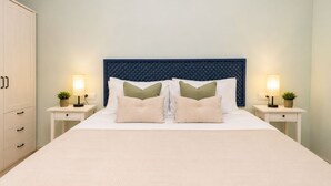 A neatly made bed with a textured white duvet, flanked by two bedside tables with lamps and small potted plants. - Coastal Living Near Estepona Marina (Estepona)