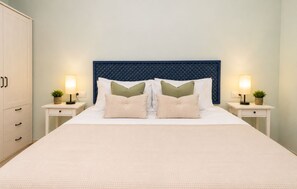 A neatly made bed with a textured white duvet, flanked by two bedside tables with lamps and small potted plants. - Coastal Living Near Estepona Marina (Estepona)