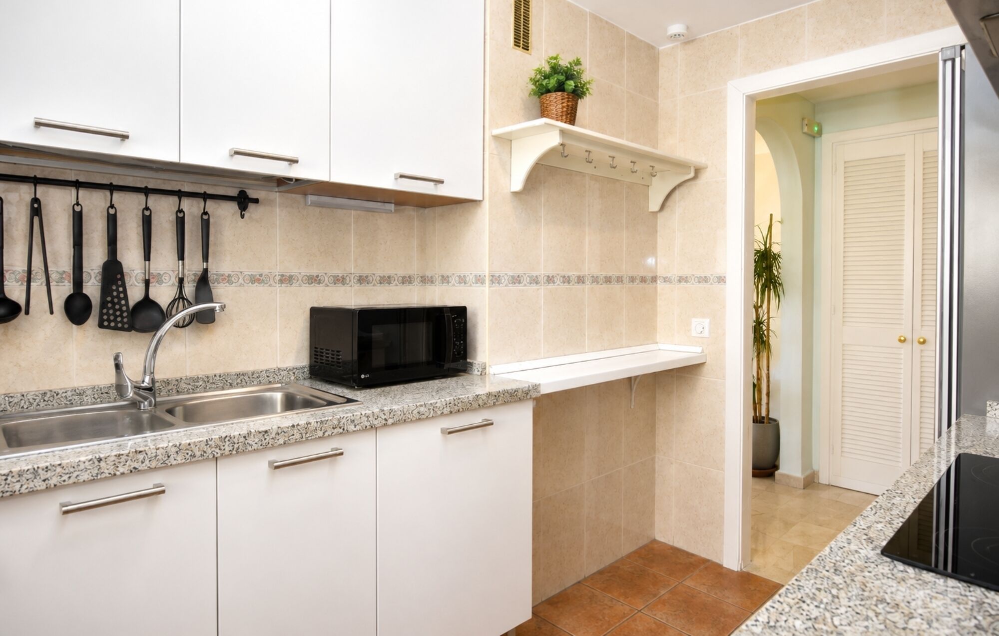 A kitchen with white cabinets, a granite countertop, a microwave, and a hanging utensil rack.