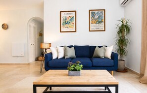 A living room with a blue sofa, a coffee table with a plant, and two framed artworks on the wall. - Coastal Living Near Estepona Marina (Estepona)