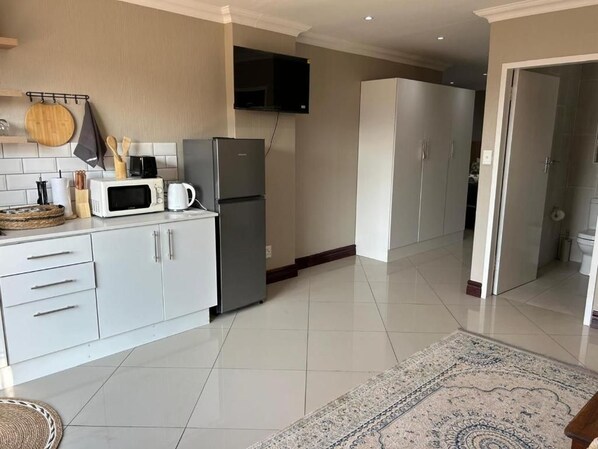A modern kitchen with white cabinets, a microwave, a refrigerator, and a flat-screen TV mounted on the wall.