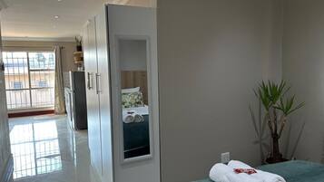 A hotel room with a bed, a bathroom, a view of the outside, and a hallway leading to other rooms.