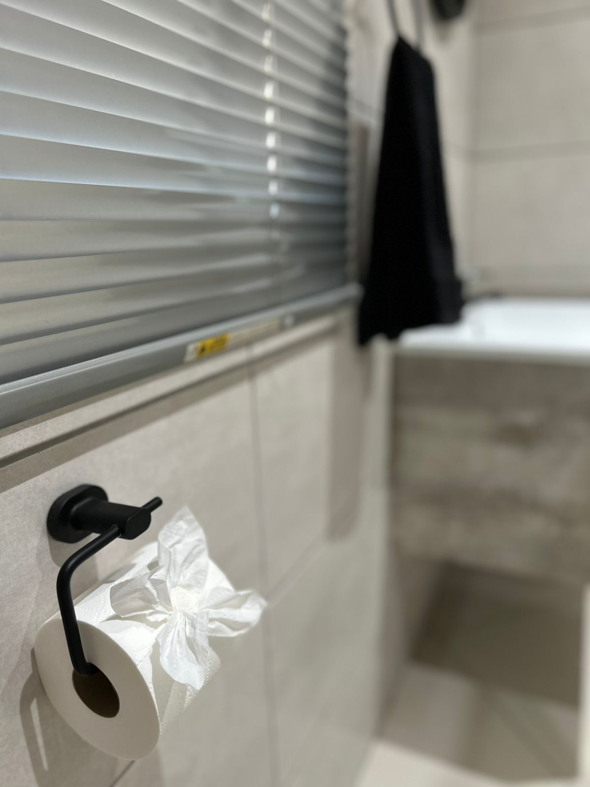 A bathroom with a toilet paper holder, a towel rack, and a shower area.